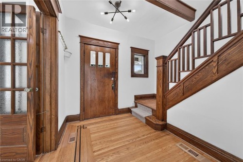 Hardwood flooring with decorative inlay, wood-paneled door with glass panels, wood-finished staircase with decorative balusters, wood beam accents, and contemporary ceiling light fixture - 229 Park Row S, Hamilton, ON 