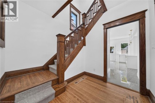 Solid wood staircase with carpeted treads, wood-finish flooring with decorative inlay, and a doorway with wood trim - 229 Park Row S, Hamilton, ON 