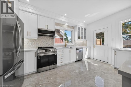 Renovated kitchen featuring white cabinetry, stainless steel appliances including a gas range and refrigerator, quartz countertops, subway tile backsplash, recessed lighting, and polished concrete flo - 229 Park Row S, Hamilton, ON 