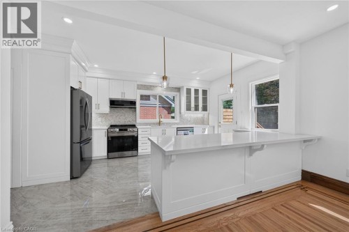 White kitchen cabinetry with gold-tone hardware, stainless steel appliances, white subway tile backsplash, and light-toned countertops - 229 Park Row S, Hamilton, ON 