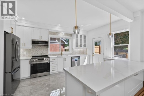 Spacious kitchen featuring white cabinetry, stainless steel appliances, a white countertop island, and pendant lighting - 229 Park Row S, Hamilton, ON 