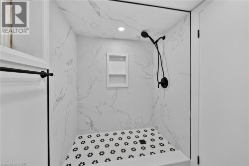 Walk-in shower with large format wall tiles, built-in recessed shelving, a black shower fixture, and a mosaic tile floor - 229 Park Row S, Hamilton, ON 