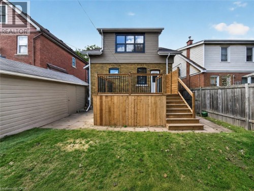 Expansive backyard with a wooden deck and stairs, featuring a privacy fence and a detached garage with siding - 229 Park Row S, Hamilton, ON 