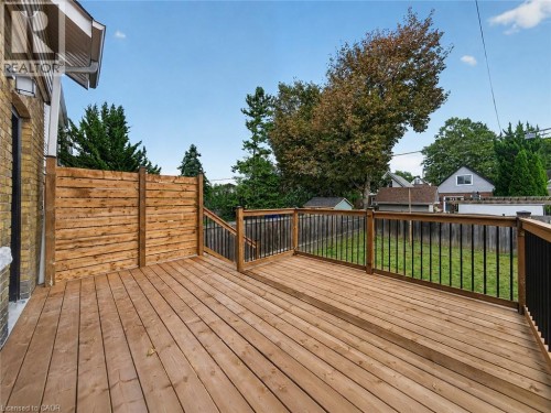 Expansive wood deck with black metal balusters and wood handrails, featuring a privacy fence and brick exterior - 229 Park Row S, Hamilton, ON 
