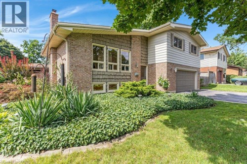 Brick exterior with white siding and decorative shingles, multiple large windows, attached garage, and a lush, landscaped front yard with ground cover - 196 Abraham Street, Cambridge, ON 