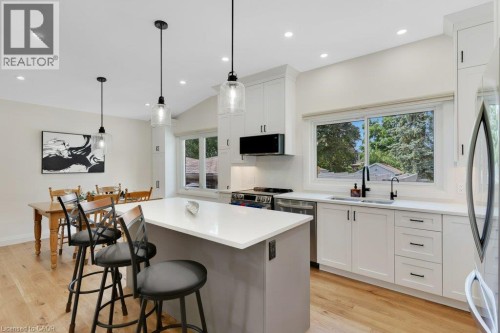Open-concept kitchen featuring an eat-at island with a light-toned countertop, white cabinetry with black hardware, stainless steel appliances, and wood-finish flooring - 196 Abraham Street, Cambridge, ON 
