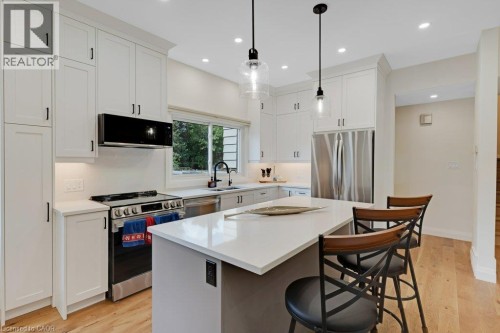 Well-appointed kitchen featuring white cabinetry, stainless steel appliances, a center island with countertop seating, and wood-finish flooring - 196 Abraham Street, Cambridge, ON 