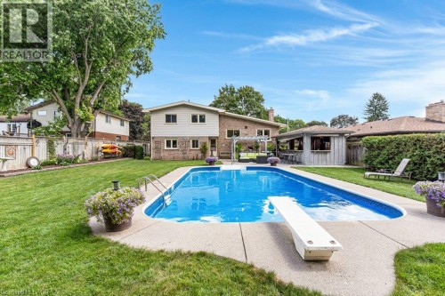 Expansive backyard featuring a large in-ground swimming pool, diving board, concrete pool deck, and a poolside bar structure - 196 Abraham Street, Cambridge, ON 