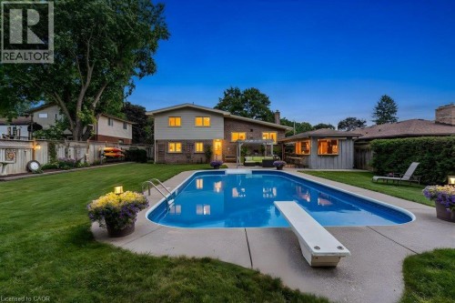 In-ground swimming pool with diving board, expansive concrete pool deck, mature landscaping, and an auxiliary structure with wood siding - 196 Abraham Street, Cambridge, ON 