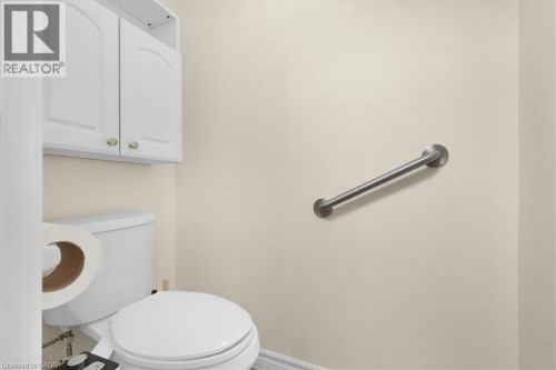 White wall cabinets with brushed nickel hardware, a white toilet, and a wall-mounted metal grab bar - 150 Bankside Drive, Kitchener, ON 