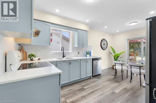 Kitchen featuring light blue cabinetry, white countertops, wood-finish flooring, a stainless steel dishwasher, and a glass sliding door - 150 Bankside Drive, Kitchener, ON 