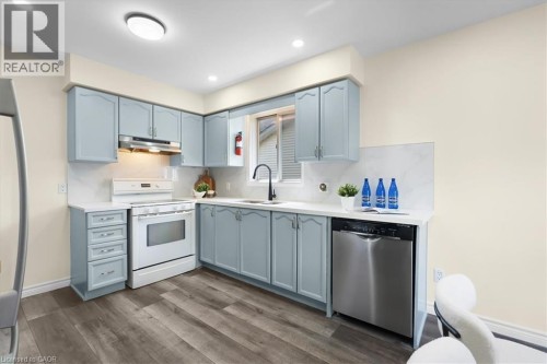 Kitchen featuring light blue cabinetry, white countertops, stainless steel dishwasher, white range, and wood-finish flooring - 150 Bankside Drive, Kitchener, ON 