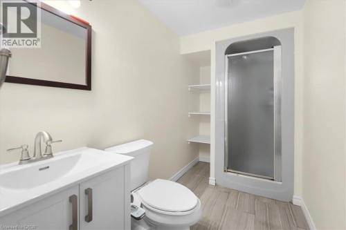 White vanity with brushed nickel hardware and a single basin sink, framed mirror, built-in shelving, glass-enclosed shower, and wood-finish flooring - 150 Bankside Drive, Kitchener, ON 