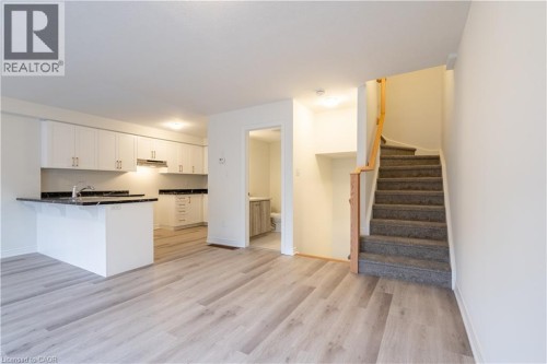 Modern kitchen with white cabinetry, dark countertops, and wood-finish flooring throughout the main level - 23 Dryden Lane, Hamilton, ON 
