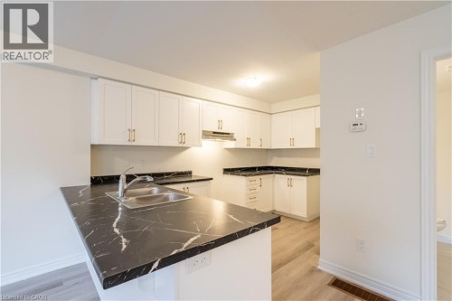 Kitchen featuring white cabinetry with gold-finish hardware, black patterned countertops, and wood-finish flooring - 23 Dryden Lane, Hamilton, ON 