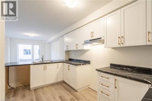 Kitchen featuring white cabinetry, gold-finish hardware, dark marble-look countertops, and wood-finish flooring - 23 Dryden Lane, Hamilton, ON 