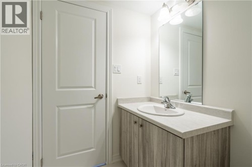 Vanity with wood-finish cabinetry, integrated sink, chrome faucet, and a wall-mounted mirror - 23 Dryden Lane, Hamilton, ON 
