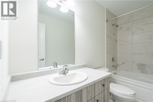 Bathroom featuring a light wood-finish vanity with an integrated sink, a large wall-mounted mirror, a tub/shower combination with subway tile surround, and a chrome faucet - 23 Dryden Lane, Hamilton, ON 