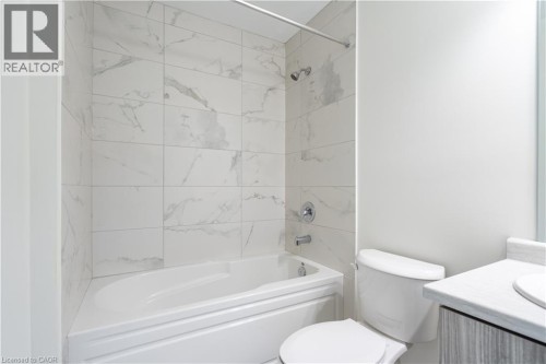 Bathtub with surrounding white and gray veined tile, chrome shower fixtures, and a toilet - 23 Dryden Lane, Hamilton, ON 