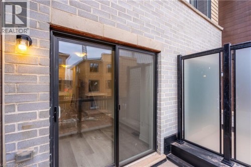 Exterior brick wall with an outdoor light fixture, sliding glass door, and privacy panels - 23 Dryden Lane, Hamilton, ON 