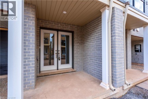 Entryway featuring light grey brick facade, white double french doors with glass panels, and a covered porch with recessed lighting - 23 Dryden Lane, Hamilton, ON 