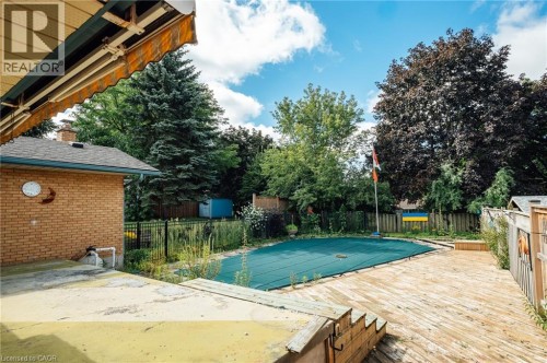 Expansive outdoor space featuring a covered pool, a large wood deck, mature trees, a brick exterior building, and a black metal fence - 229 Winfield Avenue, Waterloo, ON 