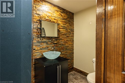 Stacked stone accent wall, vessel sink, dark wood-finish vanity, decorative mirror, and wood-finish trim - 229 Winfield Avenue, Waterloo, ON 