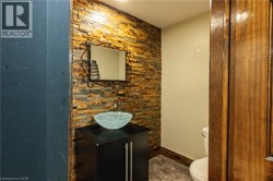 Stacked stone accent wall, vessel sink, dark wood-finish vanity, decorative mirror, and wood-finish trim - 