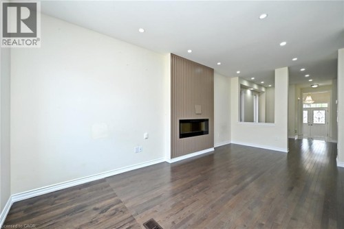 Wide plank wood-finish flooring, recessed lighting, contemporary fireplace with a fluted surround, half wall with a decorative niche, and double entry doors - 64 Maple Cider Street, Caledon, ON 