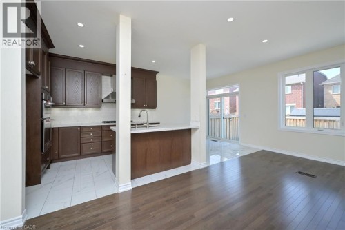 Kitchen featuring dark wood cabinetry, stainless steel appliances, a white tile backsplash, and a white countertop - 64 Maple Cider Street, Caledon, ON 