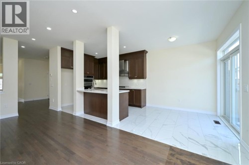 Dark wood-finish flooring, white tile flooring, recessed lighting, brown wood cabinetry, and a stainless steel range hood - 64 Maple Cider Street, Caledon, ON 