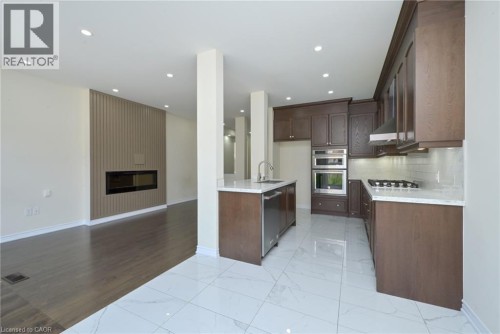 Modern kitchen featuring dark wood-finish cabinetry, stainless steel appliances, and a central island with an undermount sink - 64 Maple Cider Street, Caledon, ON 