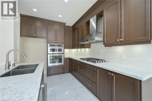 Kitchen featuring wood-finish cabinetry, light-toned countertops, subway tile backsplash, stainless steel gas range, and built-in double ovens - 64 Maple Cider Street, Caledon, ON 