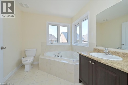 Alcove bathtub with corner windows, single vanity with an integrated sink, built-in mirror, and tile flooring - 64 Maple Cider Street, Caledon, ON 