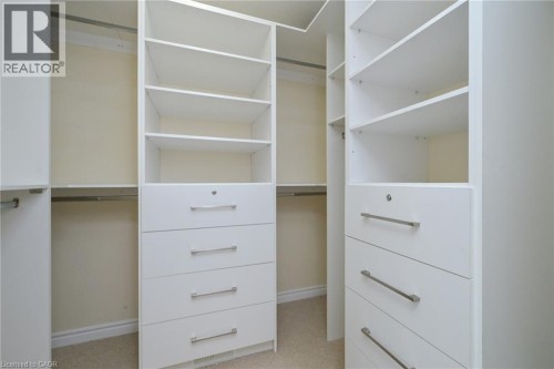 Built-in white custom closet shelving and drawer units, integrated hanging rods, and carpet flooring - 64 Maple Cider Street, Caledon, ON 