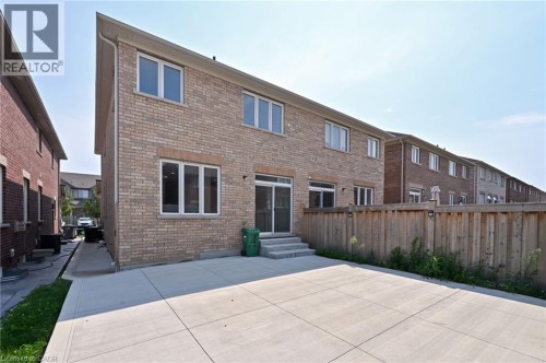 Brick exterior with multiple windows, concrete patio, and a wood fence - 64 Maple Cider Street, Caledon, ON 