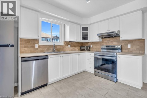 White cabinetry, stainless steel appliances, tiled backsplash, light countertops, and tiled flooring - 50 Howe Drive Unit# 19B, Kitchener, ON 