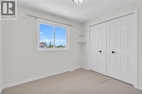 Neutral wall color, carpeted flooring, sliding window with white trim, built-in shelving, and bifold closet doors - 50 Howe Drive Unit# 19B, Kitchener, ON 