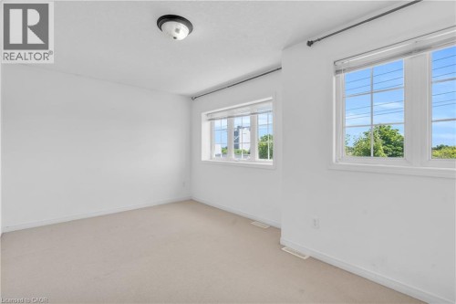 Neutral carpeted flooring, white painted walls, and multiple windows with grids - 50 Howe Drive Unit# 19B, Kitchener, ON 