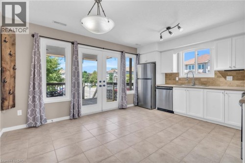 Kitchen featuring white cabinetry, stainless steel appliances, tile backsplash, and tile flooring - 50 Howe Drive Unit# 19B, Kitchener, ON 
