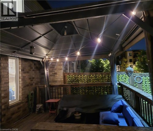 Covered deck featuring a brick exterior wall, a window with blinds, and wooden deck flooring - 1335 Countrystone Drive, Kitchener, ON 