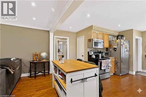 Open-concept kitchen and living space featuring warm wood-finish flooring throughout, custom white cabinetry with black hardware accents, a substantial center island with wood countertop and storage, - 1046 Shepherds Drive, Burlington, ON 