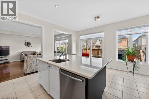 Kitchen featuring dishwasher, light tile patterned floors, white cabinetry, a kitchen island with sink, and open floor plan - 97 Sirente Drive, Hamilton, ON 