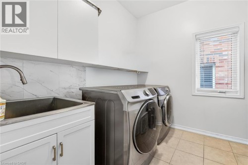 Laundry area featuring washing machine and clothes dryer, light tile patterned flooring, and cabinet space - 97 Sirente Drive, Hamilton, ON 