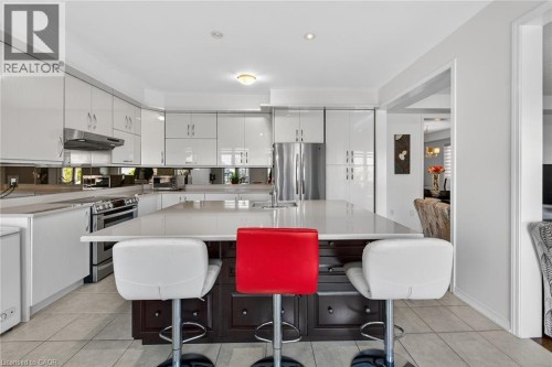 Kitchen with a kitchen island with sink, stainless steel appliances, two tone color scheme, a breakfast bar area, and light tile patterned floors - 97 Sirente Drive, Hamilton, ON 