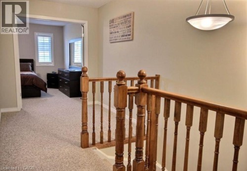 Carpeted hallway with wood banister and overhead semi-flush mount light fixture - 507 Beaumont Crescent, Kitchener, ON 