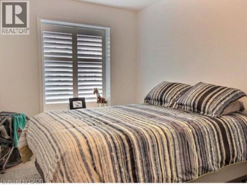 Bright bedroom showcasing neutral striped bedding, plantation shutters with adjustable louvers, and carpeted flooring - 507 Beaumont Crescent, Kitchener, ON 