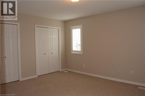 Neutral paint palette with textured carpeting, two bi-fold door closets, and a window featuring white plantation shutters - 507 Beaumont Crescent, Kitchener, ON 