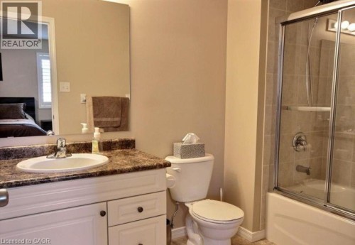 Vanity with integrated sink and patterned countertop, framed mirror, and a shower-tub combination with sliding glass doors - 507 Beaumont Crescent, Kitchener, ON 