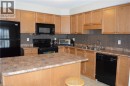 Kitchen featuring natural wood-finish cabinetry, black appliances, a central island, and a mosaic tile backsplash - 507 Beaumont Crescent, Kitchener, ON 